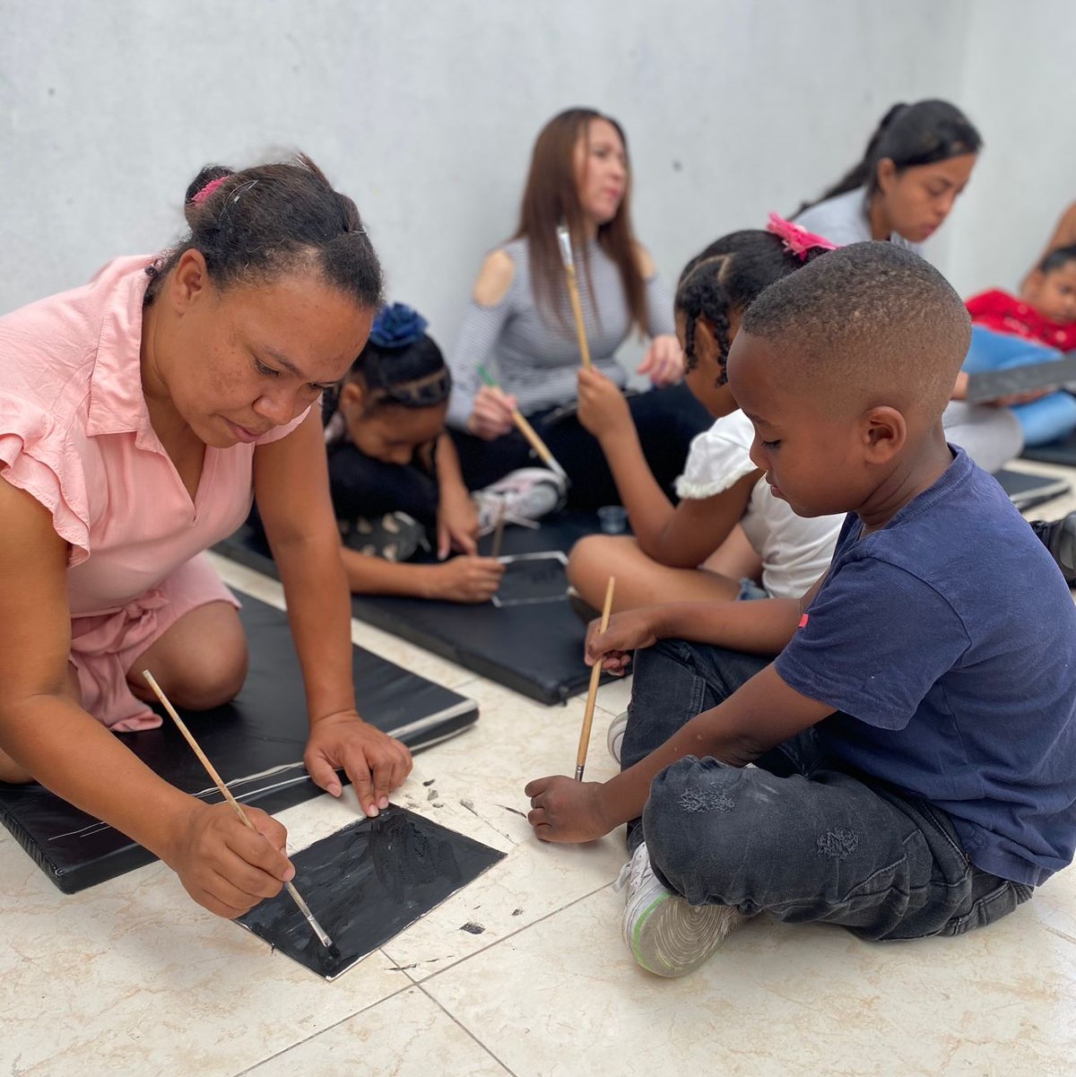 Una mujer y su hijo, sentados en el piso realizando una pintura con pincel.